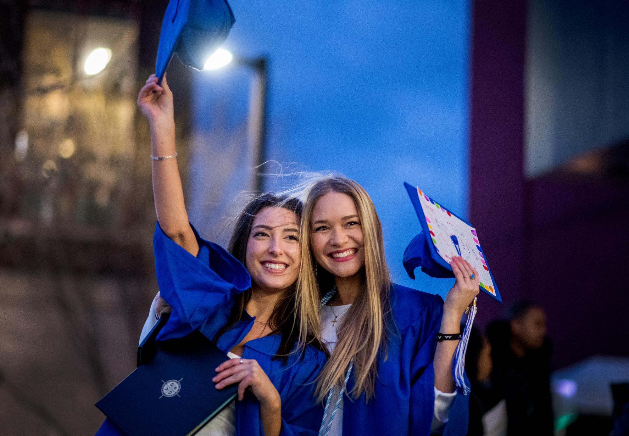 两位毕业生戴着蓝帽子，微笑着在毕业典礼上庆祝